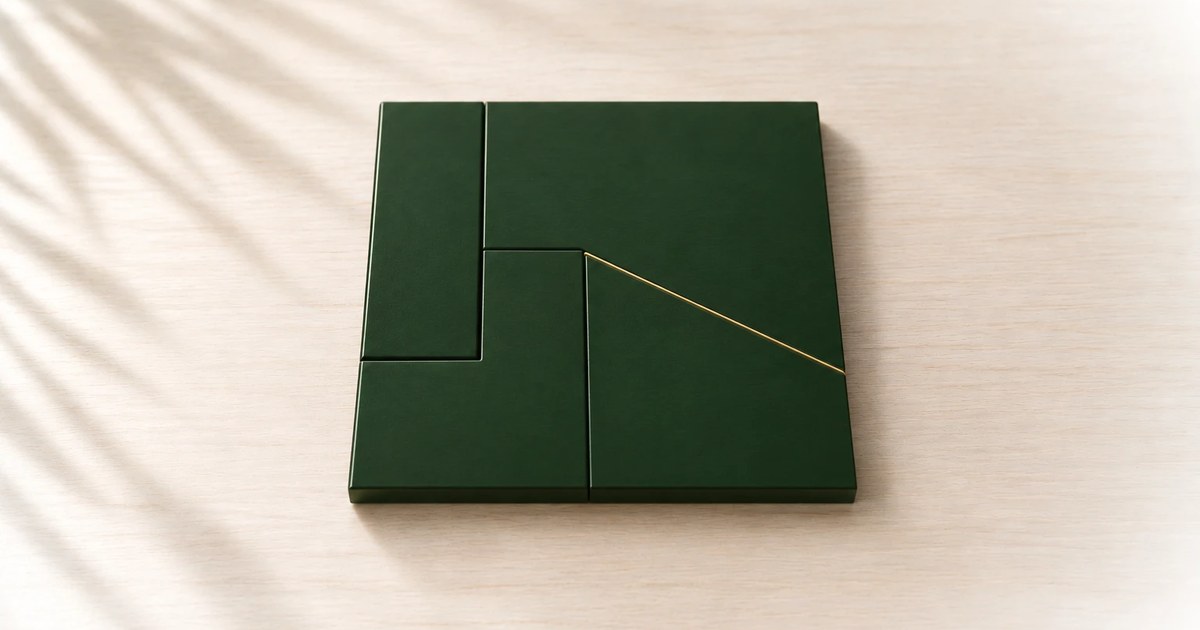 Four green wooden pieces of different shapes fitted together into one square on a pale desk.