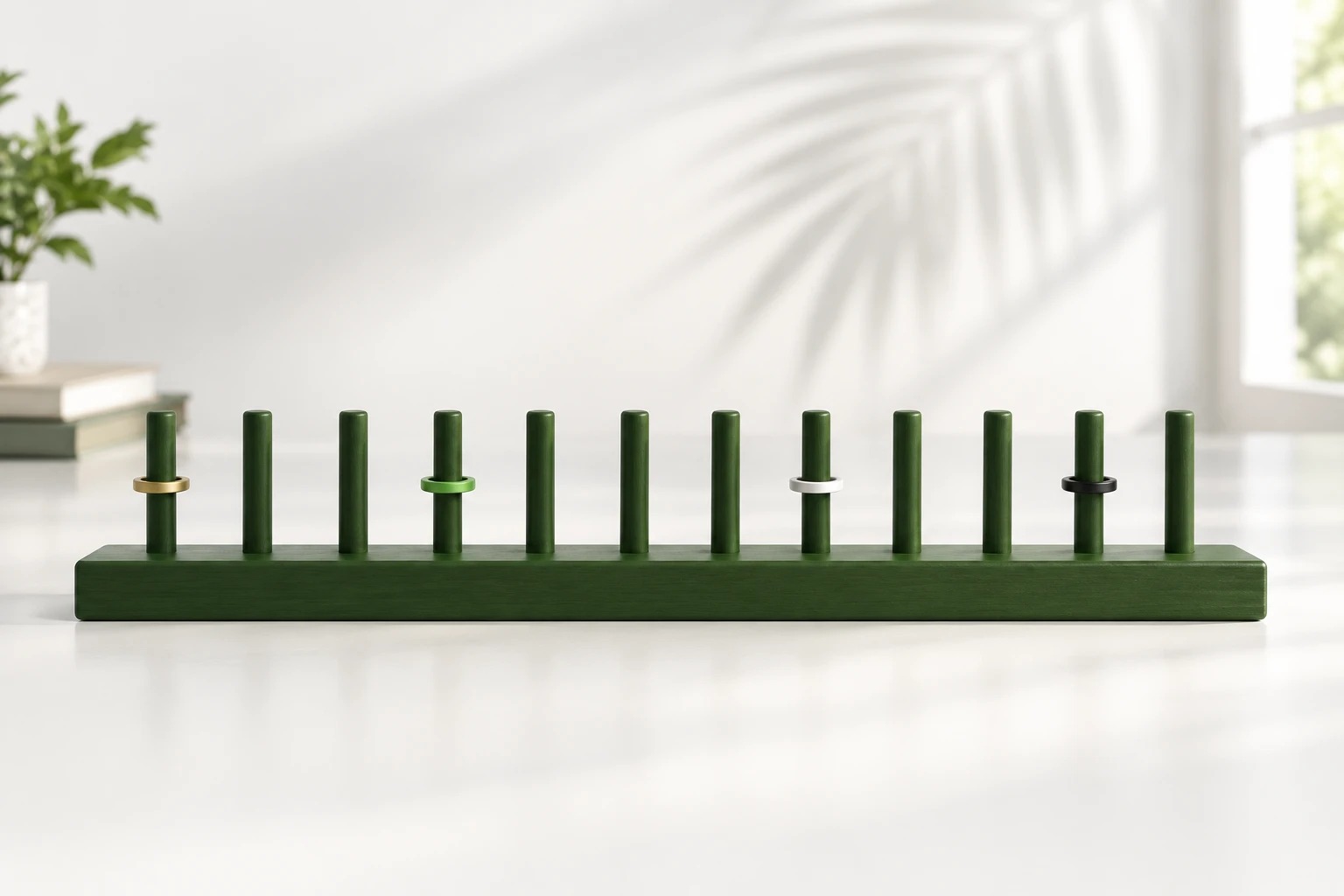 A long green rail with twelve plain pegs, four wearing coloured rings, on a white desk.